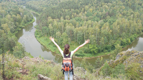 A female traveler stands with a backpack hands up. Success, luck, achievement. Travel to the Berd rocks in Russia. Novosibirsk region, summer photo