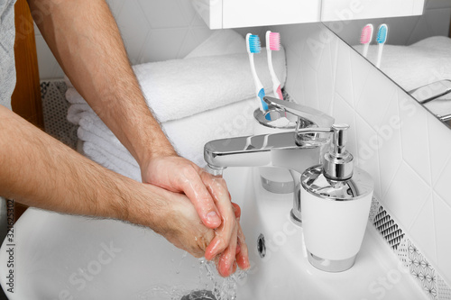 Everyday morning hygiene. Man wash his hands. Bath preparation. White interior of bathroom. Toothbrush and soap dispenser. Details of bathroom. Personal care. Measures against infection and virus