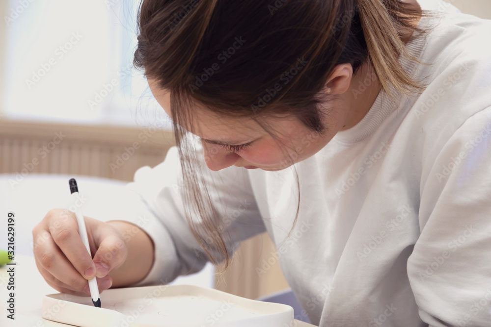 Selective focus. Close-up portrait of teenage girl indoors. She draws with a pencil, passionate about her occupation. Selective focus. Close-up portrait of teenage girl indoors. She draws with a pencil, passionate about her occupation.