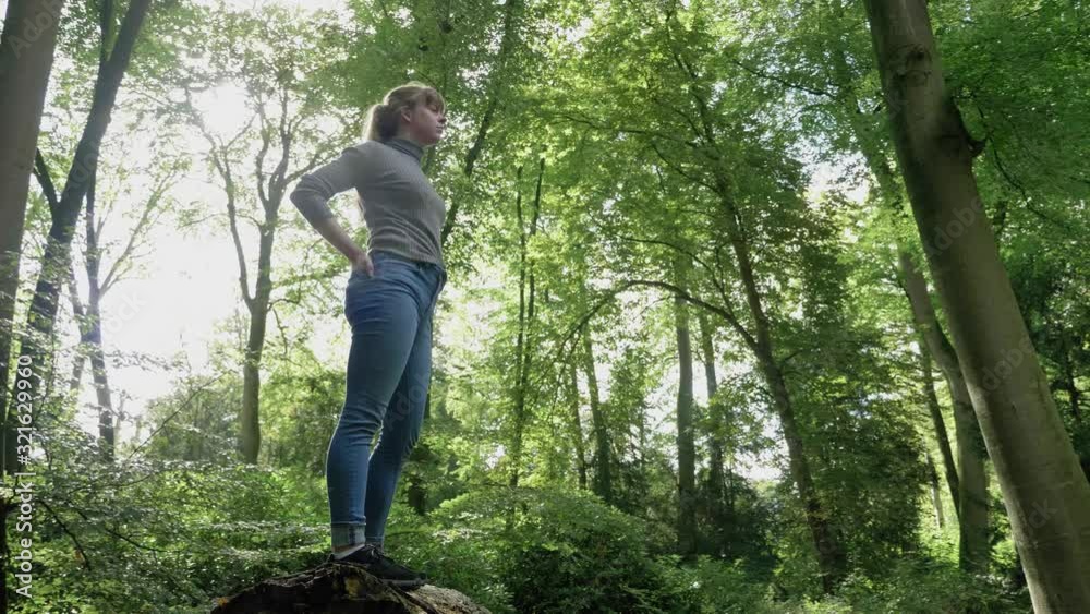 Girl stands stall on fallen log surveying forest, low angle, tracking, wide Girl stands stall on fallen log surveying forest, low angle, tracking, wide