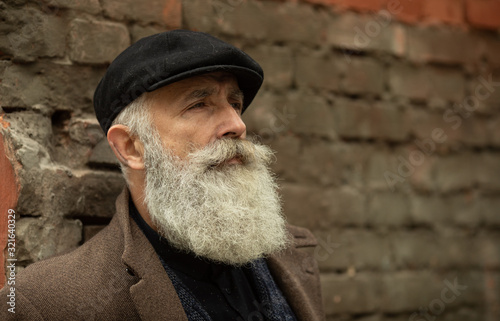 Fashionable senior man with gray hair and beard is outdoors on the street.
