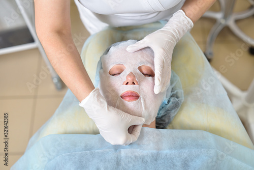 A beautician applies a mask to the face of a girl during a facial skin care procedure. Skincare and beauty concept