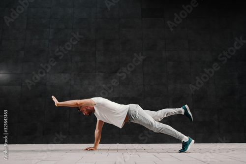 Handsome caucasian bearded man in tracksuit doing strength exercises for arms and legs on the ground.