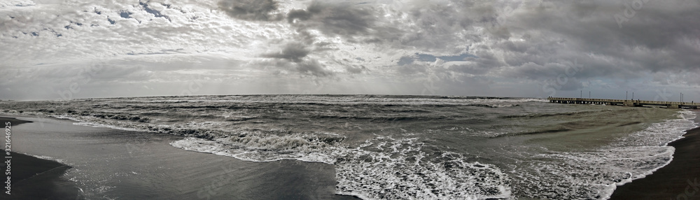 Dramatic lights and bad weather panorama over the sea, threatening waves crashing at the shore with overcast sky and sunbeams hitting the water's edge on Roman coast