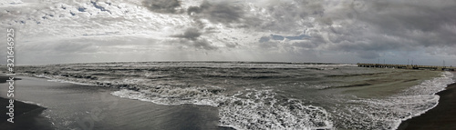 Dramatic lights and bad weather panorama over the sea, threatening waves crashing at the shore with overcast sky and sunbeams hitting the water's edge on Roman coast