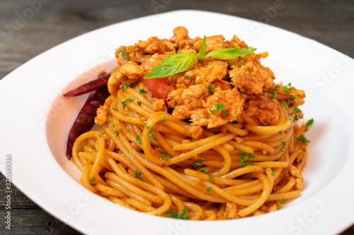 Spicy spaghetti pasta with fried chicken and chili in white dish on black wooden table.