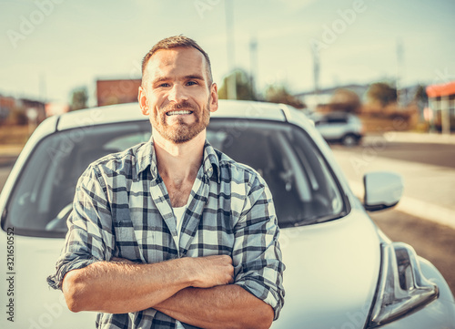 An attractive young man stands near a white car. Toned photo.