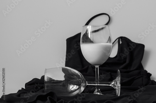 A glass with a white drink stands on a small black dress thrown on the table. The empty glass lies nearby.