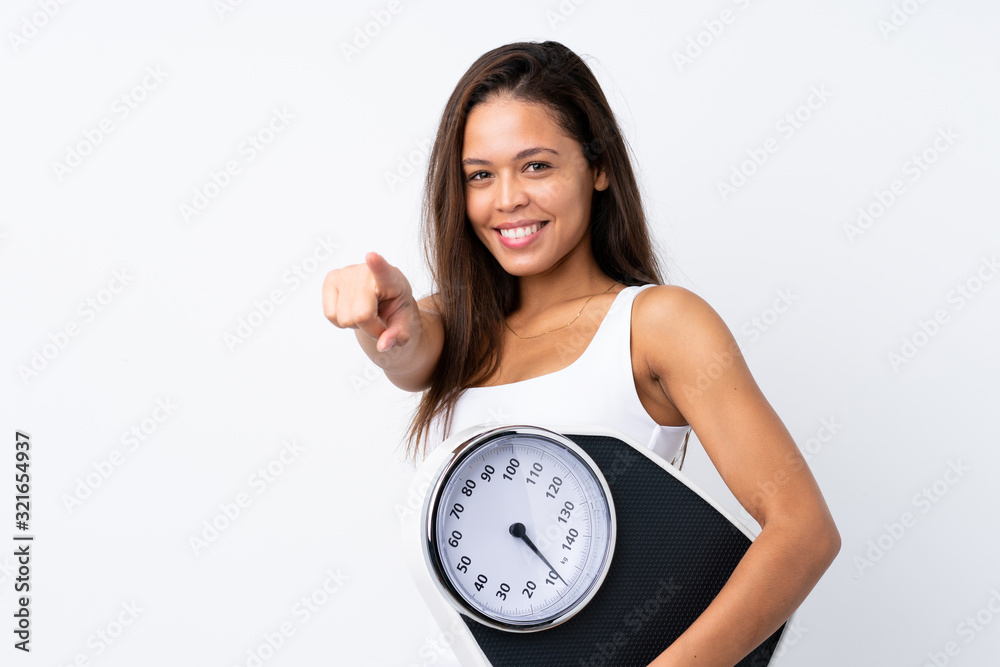 Young Brazilian girl holding a scale over isolated background holding a weighing machine and pointing to the front Young Brazilian girl holding a scale over isolated background holding a weighing machine and pointing to the front
