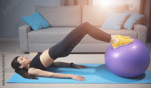 Young female practice pilates do bridge with fitball lying on floor in living room
