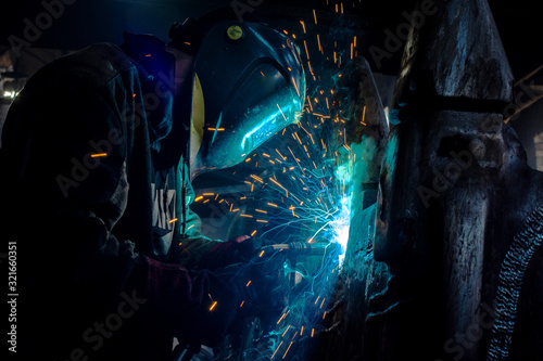 Side view of welder in protective helmet welding metal detail with sparks at factory 