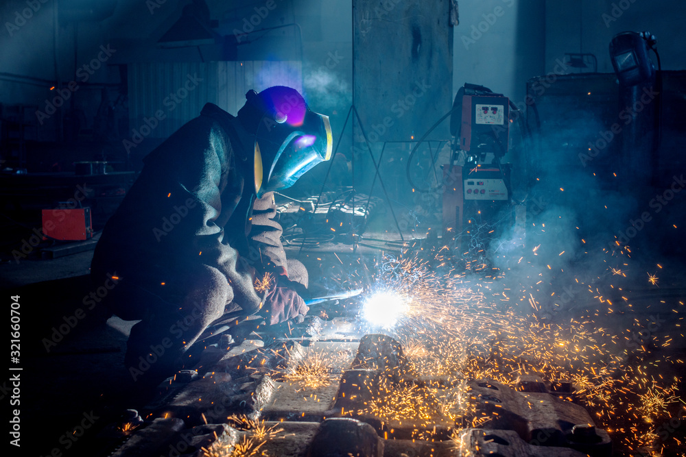 Side view of welder in protective helmet welding metal detail with sparks at factory Side view of welder in protective helmet welding metal detail with sparks at factory