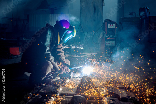 Photos Side view of welder in protective helmet welding metal detail with sparks at fac