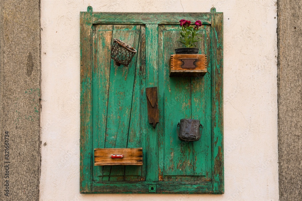 Close-up of a stone wall with a hanging green wooden plank and recovery items, Italy