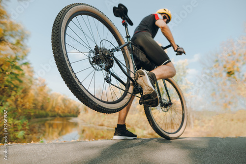 Fototapeta Naklejka Na Ścianę i Meble -  Action photo of a cyclist doing the trick in the park, lifting the rear wheel up. A man is extreme riding on the road in the park. Closeup photo of an extreme cyclist