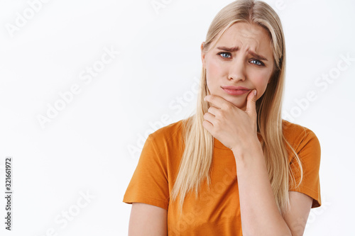 Obraz na plátně Skeptical displeased young blond girl, furrowed eyebrows and squinting, touch ch