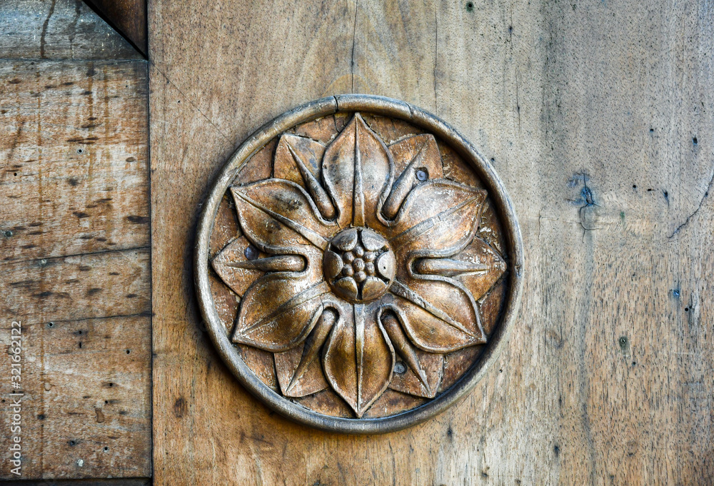 Close-up of an old wooden door with carved circular floral decoration, Italy