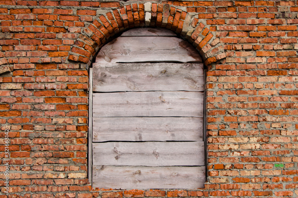 Old red brick masonry and arched window opening clogged with boards. Background for design.