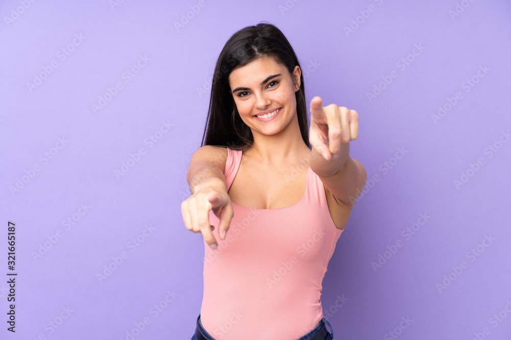 Young woman over isolated purple background points finger at you while smiling Young woman over isolated purple background points finger at you while smiling