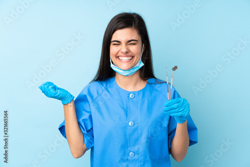 Young woman dentist holding tools over isolated blue background laughing