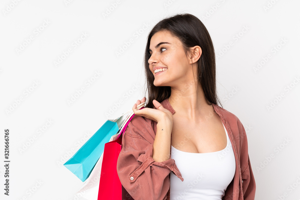 Young woman over isolated white background holding shopping bags and looking back Young woman over isolated white background holding shopping bags and looking back
