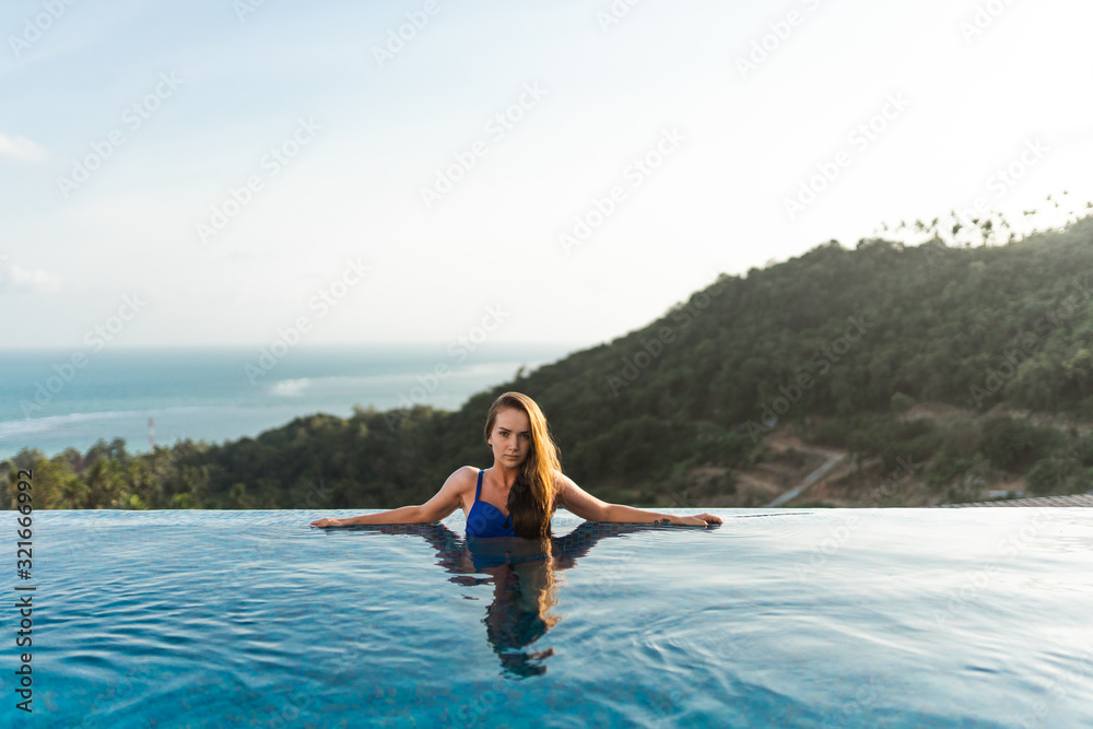 Beautiful girl in shorts and a bathing suit in a luxury villa by the pool with wine and in a hat takes cover from the sun. View of palm trees and the sea. Thailand, Samui Beautiful girl in shorts and a bathing suit in a luxury villa by the pool with wine and in a hat takes cover from the sun. View of palm trees and the sea. Thailand, Samui