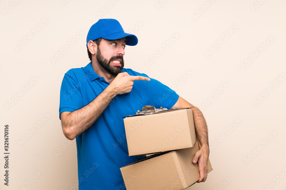 Delivery man with beard over isolated background frightened and pointing to the side Delivery man with beard over isolated background frightened and pointing to the side