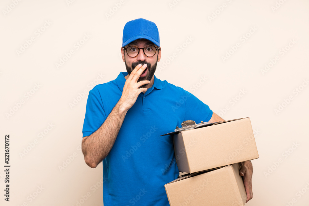 Delivery man with beard over isolated background with glasses and surprised Delivery man with beard over isolated background with glasses and surprised