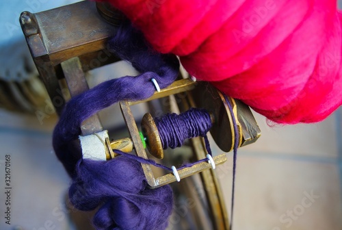 Close up of flyer with red and blue raw merino wool from old wooden spinning wheel