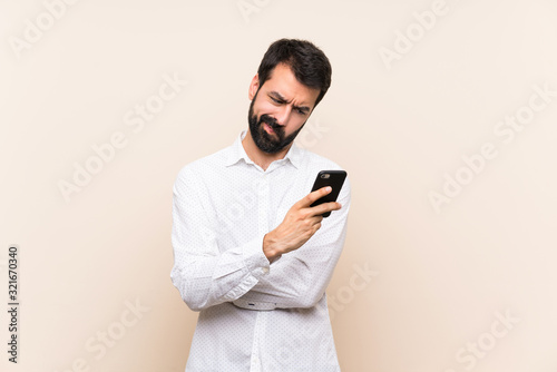 Young man with beard holding a mobile feeling upset
