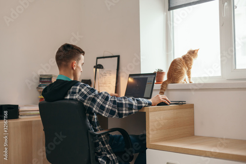 Teenage boy doing homework using computer sitting by desk in room alone photo