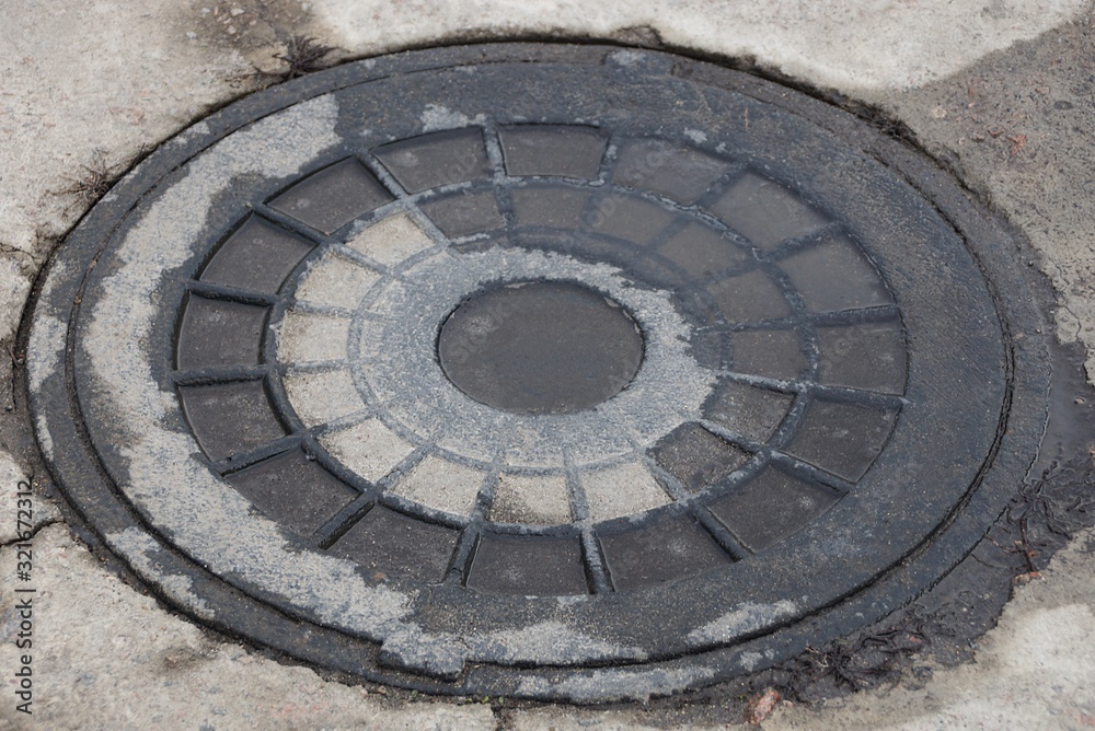 one old and wet iron sewer manhole lies on gray asphalt on the street