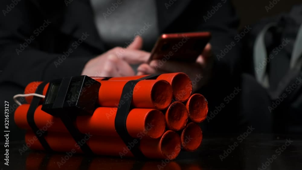 Female hands of terrorist take red bomb and put explosives in bag close-up on black background.