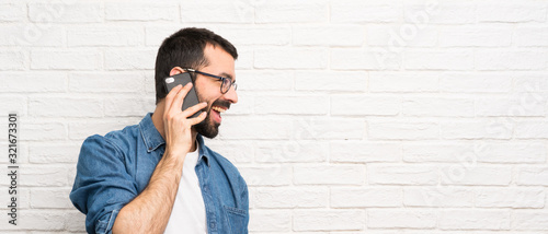 Handsome man with beard over white brick wall keeping a conversation with the mobile phone