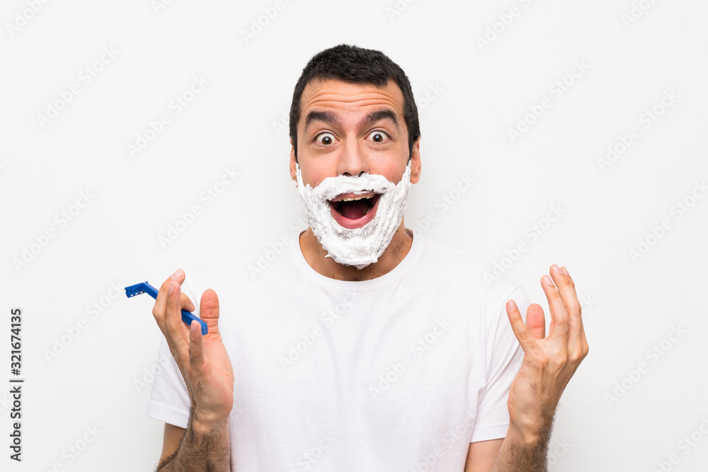 Man shaving his beard over isolated white background with shocked facial expression