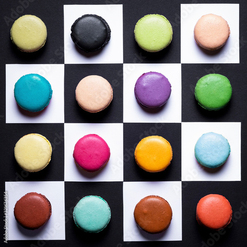 Creative layout of colorful macaroons on chessboard background. Multicolor variety of french almond macaron cookies. Dessert, sugar, bakery creative, playful concept.Alternatvie chess game.Food design