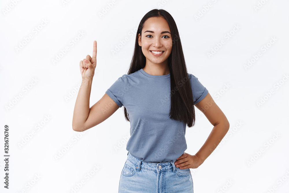 Upbeat, carefree lively smiling asian woman brunette in casual t-shirt, hold hand on waist with positive attitude pointing finger up, showing one, grinning, give advice what buy, promote product Upbeat, carefree lively smiling asian woman brunette in casual t-shirt, hold hand on waist with positive attitude pointing finger up, showing one, grinning, give advice what buy, promote product