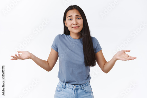 Girl saying sorry cant decide or think up solution, shrugging and spread hands sideways hopeless, smiling with apologizing innocent expression, being unsure or doubtful, cant tell, white background
