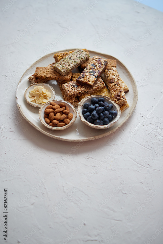 Mixed composition of energy nutrition bar, granola on ceramic plate over white background