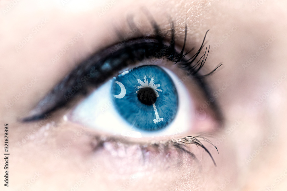 Fototapeta premium Flag of South Carolina state of the United States of America reflects in a woman blue eye - election, sport, hope, young, generation, american football, basket, emotion
