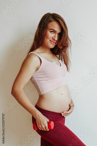 A happy, young, pregnant girl with a rounded belly poses while playing sports. Health care before childbirth.