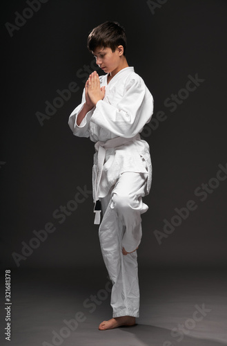 a teenager dressed in martial arts clothing poses on a dark gray background, a sports concept