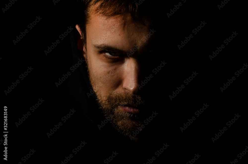 male evil face. portrait of evil on a black background. Dark portrait of a man looking like a devil. the criminal is hiding