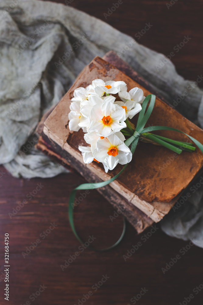 Naklejka premium Small Bouquet of Paperwhite Nacissus tied with Green Ribbon on Vintage Books
