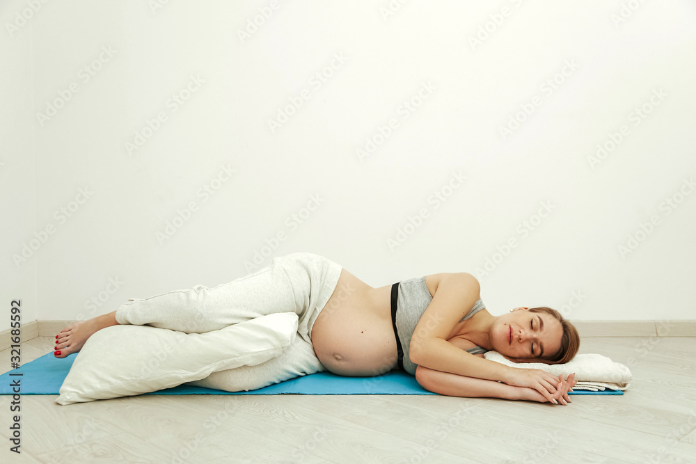 Obraz premium A pregnant girl, in the last month of pregnancy, lies on a soft rug in the room. Young mother is resting before childbirth.