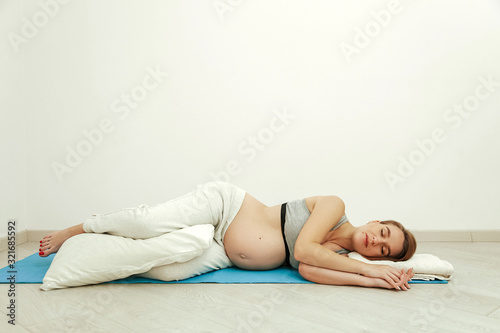 A pregnant girl, in the last month of pregnancy, lies on a soft rug in the room. Young mother is resting before childbirth.