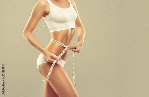  Perfect slim toned young body of the girl . An example of sports , fitness or plastic surgery and aesthetic cosmetology.Woman measuring her waist over white background