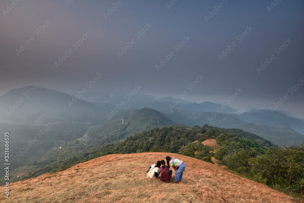 Three girl is sitting on a hill top with mountain range background in an evening