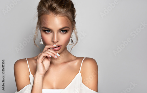 Beautiful model girl with blond hair . Woman with a high hairstyle is wearing a white top.Fashion makeup and cosmetics . Big golden shine  earrings jewelry .