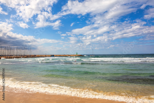 Tel Aviv seaside beautiful view. Surfers enjoy the sea surf on sunny day. Yachts in Marina and lighthouse on horizon. Mediterranean Sea coastal area in Tel Aviv